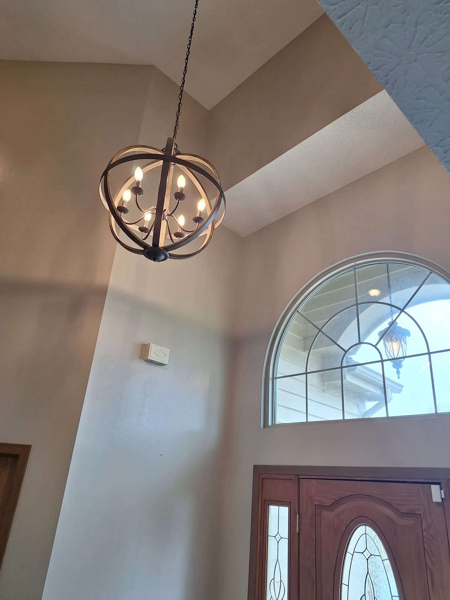 Two-story foyer with arched window and orb chandelier painted soft beige